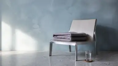 Et sammenfoldet uldtæppe og et glas vand på en lav stol viser den rolige landing efter intensitet.