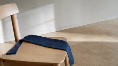 En blød blindfold ligger åben ved siden af en stabil stol i dagslys, klar til at blive valgt til eller fra.