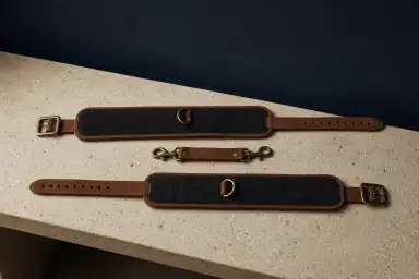 To polstrede ruskindsmanchetter ligger helt udfoldede med frie spænder og D-ringe omkring en løs connector med to kroge.