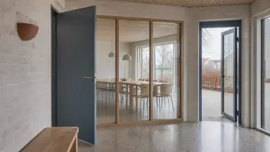 En oplyst fællesdør med synligt håndtag, ryddelig opslagstavle uden tekst og en fri vej tilbage gør vurderingen af rammen konkret.