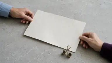 To voksne hænder holder hver sin side af et løst, ulæseligt dokument; en åben clips viser, at aftalen kan ændres.